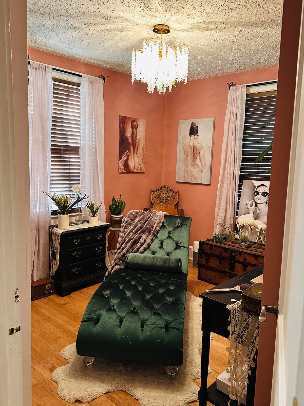 The treatment room at Willow Vale Aesthetics, seen from the doorway: an emerald velvet chaise under a crystal chandelier, terracotta walls.
